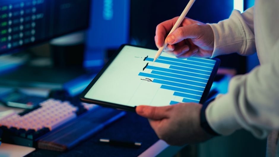 A person using a stylus on a tablet showing a business graph in an office setting.